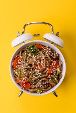 Çalar saatin arka planında et, sos ve sebzeli İtalyan makarnası. Makarna yemek için kavramsal arka plan zamanı