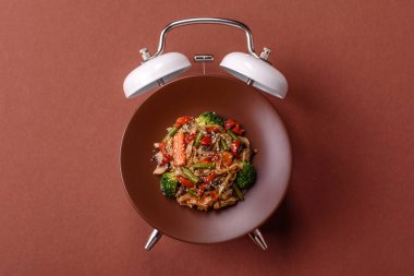 Çalar saatin arka planında et, sos ve sebzeli İtalyan makarnası. Makarna yemek için kavramsal arka plan zamanı