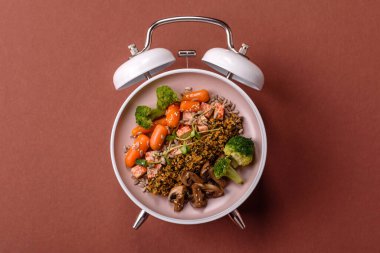 Çalar saatin arka planında kinoalı, sebzeli, etli ve yumurtalı vejetaryen salatası ya da kase. Vejetaryen yemeği yemek için kavramsal geçmiş zamanı