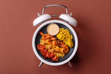 Çalar saatin arka planında kinoalı, sebzeli, etli ve yumurtalı vejetaryen salatası ya da kase. Vejetaryen yemeği yemek için kavramsal geçmiş zamanı