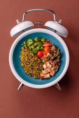 Çalar saatin arka planında kinoalı, sebzeli, etli ve yumurtalı vejetaryen salatası ya da kase. Vejetaryen yemeği yemek için kavramsal geçmiş zamanı