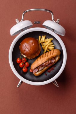 Sosisli sandviç, sosisli, hardal, mayonez ve ketçap. Çalar saat skorbordunda tabakla fast food yeme zamanı.