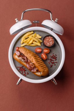 Sosisli sandviç, sosisli, hardal, mayonez ve ketçap. Çalar saat skorbordunda tabakla fast food yeme zamanı.