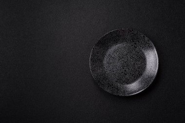Yemek için boş yuvarlak siyah tabak, yemek masasında mutfak gereçleri. Koyu arkaplanda boş tabak