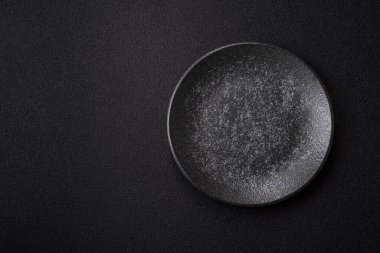 Yemek için boş yuvarlak siyah tabak, yemek masasında mutfak gereçleri. Koyu arkaplanda boş tabak