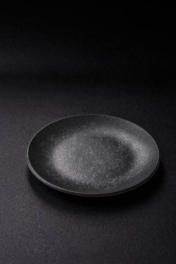 Yemek için boş yuvarlak siyah tabak, yemek masasında mutfak gereçleri. Koyu arkaplanda boş tabak