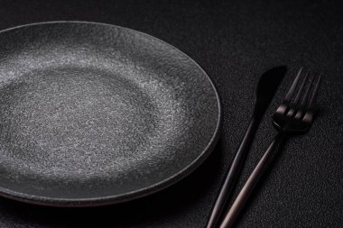 Yemek için boş yuvarlak siyah tabak, yemek masasında mutfak gereçleri. Koyu arkaplanda boş tabak