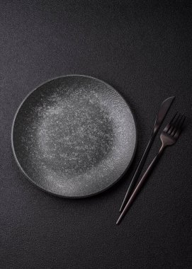 Yemek için boş yuvarlak siyah tabak, yemek masasında mutfak gereçleri. Koyu arkaplanda boş tabak