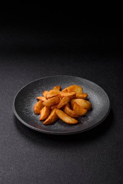 Biberiye, peynir, tuz ve baharatlı ızgara patates dilimleri. Koyu beton zeminde fırında patates dilimleri.