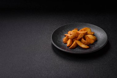 Biberiye, peynir, tuz ve baharatlı ızgara patates dilimleri. Koyu beton zeminde fırında patates dilimleri.