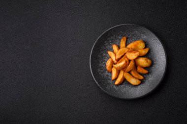 Biberiye, peynir, tuz ve baharatlı ızgara patates dilimleri. Koyu beton zeminde fırında patates dilimleri.