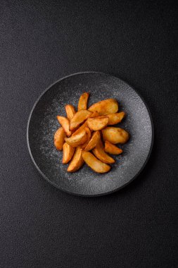 Biberiye, peynir, tuz ve baharatlı ızgara patates dilimleri. Koyu beton zeminde fırında patates dilimleri.