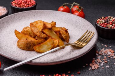 Biberiye, peynir, tuz ve baharatlı ızgara patates dilimleri. Koyu beton zeminde fırında patates dilimleri.