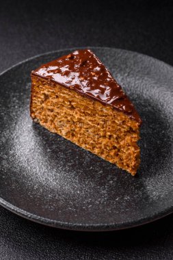 A slice of sweet layered cake covered in chocolate with nuts and caramel. A slice of chocolate cake as a food background for your design.