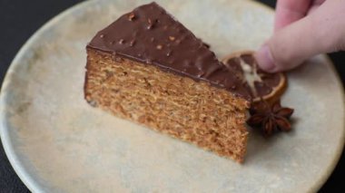 A slice of sweet layered cake covered in chocolate with nuts and caramel. A slice of chocolate cake