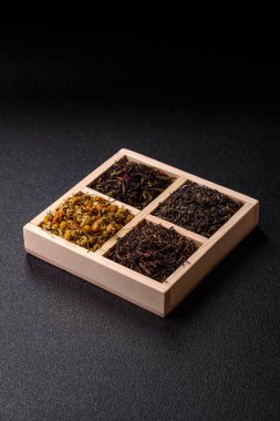 A wooden box with several types of dried tea, green, black, fruit, and chamomile. Dry tea in the box as a backdrop for your design.