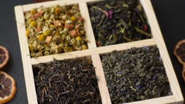 A wooden box with several types of dried tea, green, black, fruit, and chamomile. Dry tea in the box as a backdrop for your design.