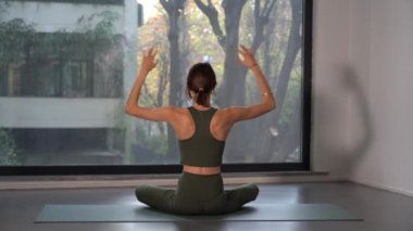 Küçük hanım pencerenin yanında yoga meditasyon egzersizleri yapıyor. Gittikçe daha fazla insan evinde ya da spor yaparak kendini kişisel refahına adıyor.
