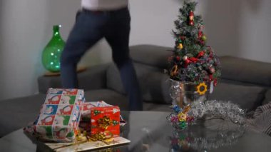 Single man spends Christmas day at home alone and Christmas tree - dancing happily to celebrate the holidays alone in sofa living room
