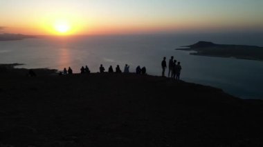 Spain, Lanzarote, Canary island - drone view of people silhouette on amazing sunset in Mirador del Rio on the Risco de Famara - Tourist looking the sun and the ocean sea - Travel in Lanzarote