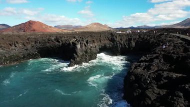 Europe, Spain, Lanzarote, Canary Islands - Los Hervideros volcanic coastline known for waves crashing into sea black caves  - picturesque landscape with a red volcano - tourist attraction