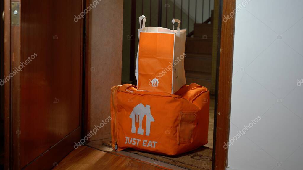Europe, Italy, Milan 2023 - Just Eat food delivery arrives home in the apartment where the man is ready for dinner - home delivery on the landing outside the door