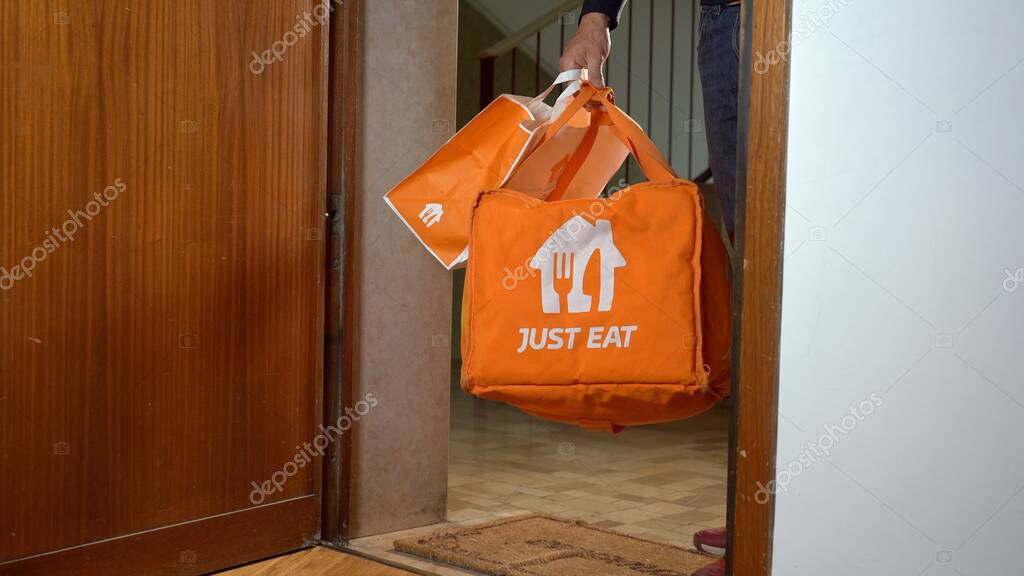 Europe, Italy, Milan 2023 - Just Eat food delivery arrives home in the apartment where the man is ready for dinner - home delivery on the landing outside the door