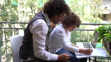 Baba ve oğlu, 9 yaşında ilkokul öğrencisi. Yaz tatili için ödev yapıyor. Ev balkonunda dizüstü bilgisayarı olan çocukluk dönemi öğrencisi.