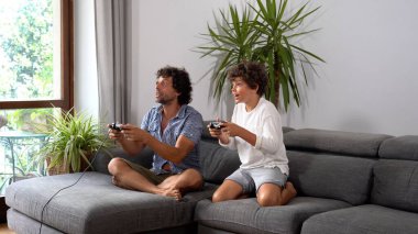 Genç baba ve oğul evde video oyunu oynuyorlar..