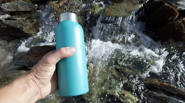 filling the water bottle in a mountain stream - glacier thaw and drinking water in the river - no plastic use and eco-friendly choice for the environment - Save the Planet