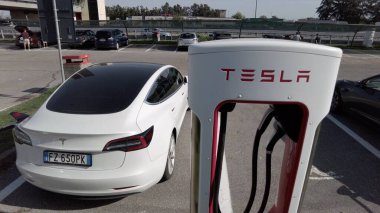Tesla elektrikli otomobil şehrin merkezindeki modern bir elektrik şarj istasyonunda bataryasını şarj ediyor - yeni sürdürülebilir elektrik hareketliliği - küresel ısınma