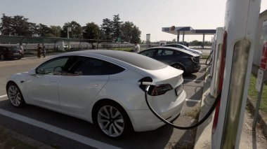 Tesla elektrikli otomobil şehrin merkezindeki modern bir elektrik şarj istasyonunda bataryasını şarj ediyor - yeni sürdürülebilir elektrik hareketliliği - küresel ısınma