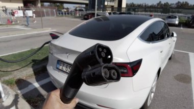 Tesla elektrikli otomobil şehrin merkezindeki modern bir elektrik şarj istasyonunda bataryasını şarj ediyor - yeni sürdürülebilir elektrik hareketliliği - küresel ısınma