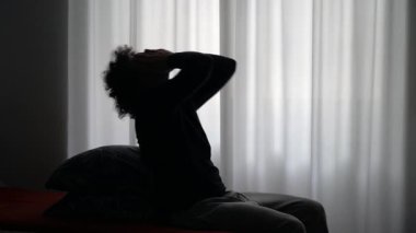 Yatakta başı tutarak oturan bunalımlı bir adam. Keder krizi ayrılığı yorgunluk baş ağrısı tükenmesi 