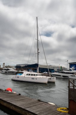 Bir Lagoon 440 katamaran arka planda Sunseeker üretim tesisinin bir kısmıyla donatılmış motor gücüyle Poole rıhtımında geziniyor.