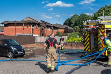 Dorset and Wiltshire firefighters clearing away hoses after a house fire in Swindon with the fire damaged terraced houses in the background