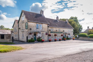 The Bell on the Common, an old stone built pub in the village of Broughton Gifford in Wiltshire on a sunny day with patches of white cloud in the sky