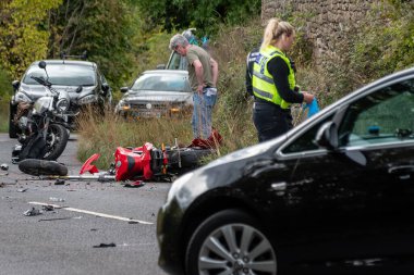 Winsley, Wiltshire, İngiltere, 25 Eylül 2022, olay yerini inceleyen bir kamu görevlisi ve acil servis personeliyle çarpıştıktan sonra yolda ağır hasar görmüş bir motosiklet.