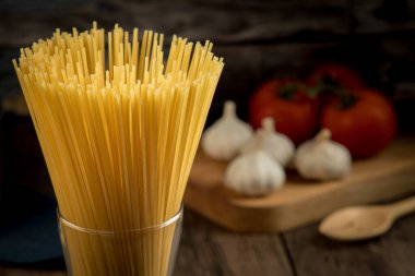 Bardakta spagetti, domates, mantar, kekik ve ahşap bir masaya yerleştirilmiş çeşitli baharatlar gibi spagetti yapmak için çeşitli malzemeler..