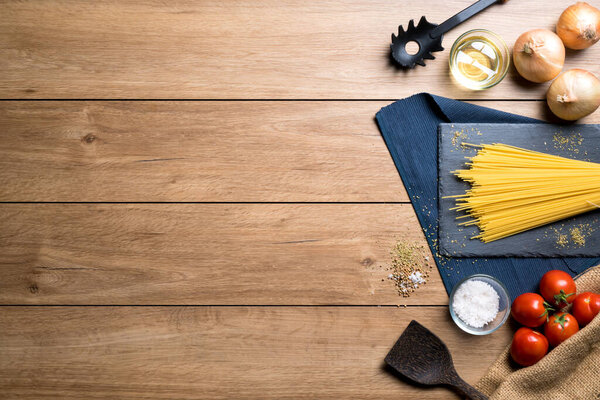 Various ingredients for making spaghetti such as spaghetti, tomatoes, oregano and various seasonings placed on a wooden table, with copy space, top view.