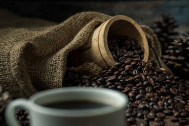 Beyaz kahve fincanındaki sıcak kahve ve etrafına bir sürü kahve çekirdeği ve sıcak, açık atmosferli, koyu arkaplanda fotokopi alanı olan ahşap bir masaya kraker..