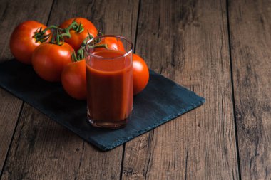 Bardakta domates suyu ve yanında da ahşap bir masada taze domates suyu.