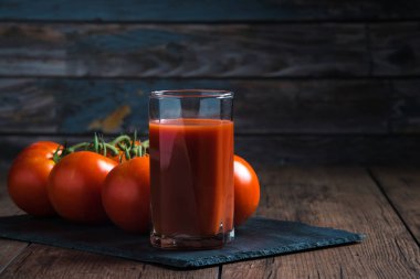 Bardakta domates suyu ve yanında da ahşap bir masada taze domates suyu.