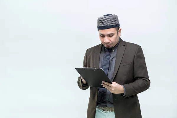 オフィスのスーツを着たアジア系イスラム教徒の男性がクリップボードの仕事情報を確認しています — ストック写真