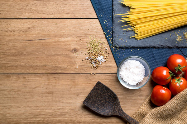 Various ingredients for making spaghetti such as spaghetti, tomatoes, oregano and various seasonings placed on a wooden table, with copy space, top view.