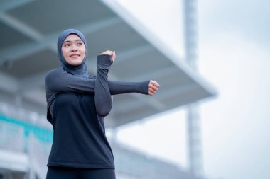 Siyah tesettürlü genç bir Asyalı Müslüman kadın sabah bir stadyumda egzersiz yapıyor ve koşuyor. Modern Müslüman kadın kavramı, Müslüman kadın spor kavramı, İslam