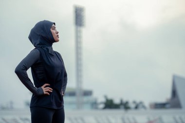 Siyah tesettürlü genç bir Asyalı Müslüman kadın sabah bir stadyumda egzersiz yapıyor ve koşuyor. Modern Müslüman kadın kavramı, Müslüman kadın spor kavramı, İslam