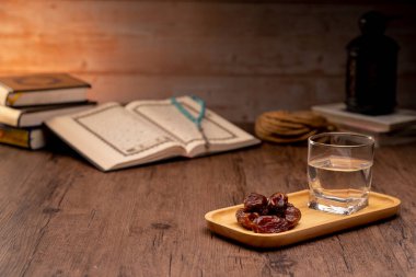 Birçok hurma kabı ve bardak su üzerindedir ve Kur 'an dünyanın dört bir yanındaki ramazan Müslümanları konseptiyle iftar zamanını beklemek için ahşap masalardadır..