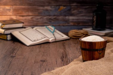 Kutsal Kur 'an ve tahtadan bir sehpanın içindeki tahtadan bir kase pirinç, İslami sadaka kavramı. Müslümanlar yoksullara ve muhtaçlara yardım etsin. Mülkiyet, gelir ve fitne için kavramsal çekim.