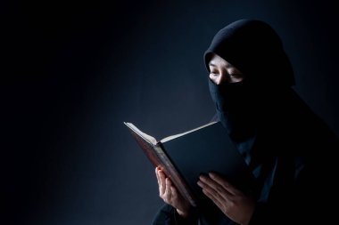 Portrait Asian Muslim woman standing and reading the Quran and appreciates and faith The Holy Al Quran with written Arabic calligraphy meaning of Al Quran, Arabic word translation: The Holy Al Quran. clipart